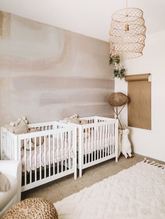 a chic twin nursery with a watercolor wall, white furniture, a rattan chandelier and rattan and paper touches