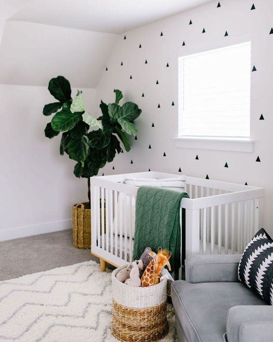 a contemporary gender neutral nursery with a geometric wall, neutral furniture, green and neutral textiles is welcoming