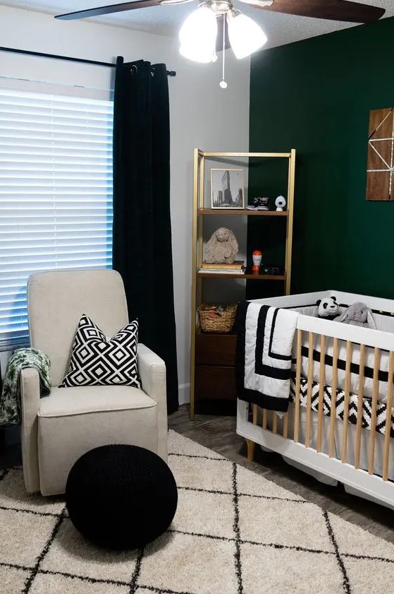 a contrasting mid century modern nursery with a dark green accent wall, a gold shelving unit, a neutral crib, a grey chair, a black pouf and black and white textiles