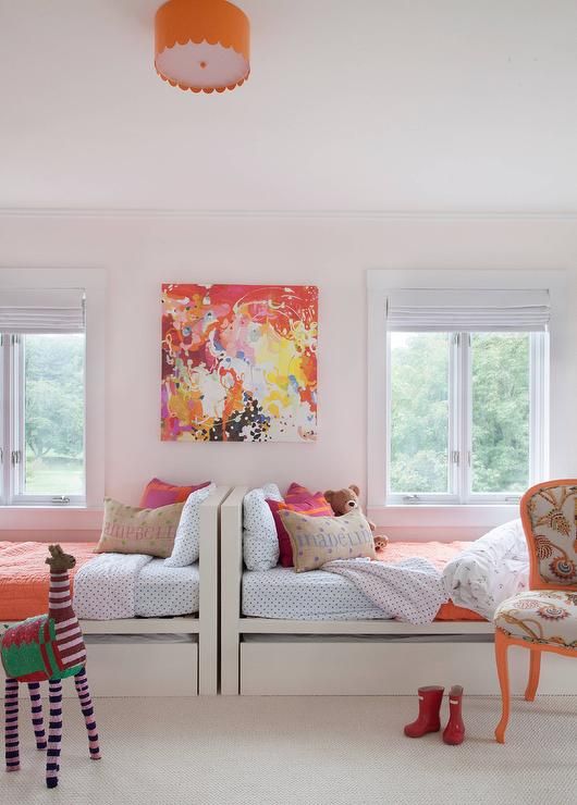 a cool and bold shared girls' bedroom with white beds, a bright chair, a colorful artwork and bedding, an orange pendant lamp and a toy