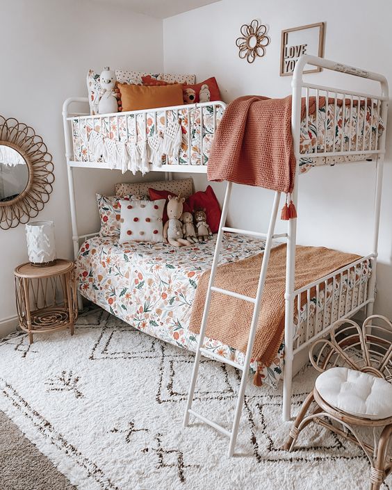 غرف بنات مشتركة A-cool-boho-shared-girls-bedroom-with-a-white-metal-bunk-bed-floral-print-bedding-a-printed-rug-a-rattan-chair-and-a-nightstand-some-art