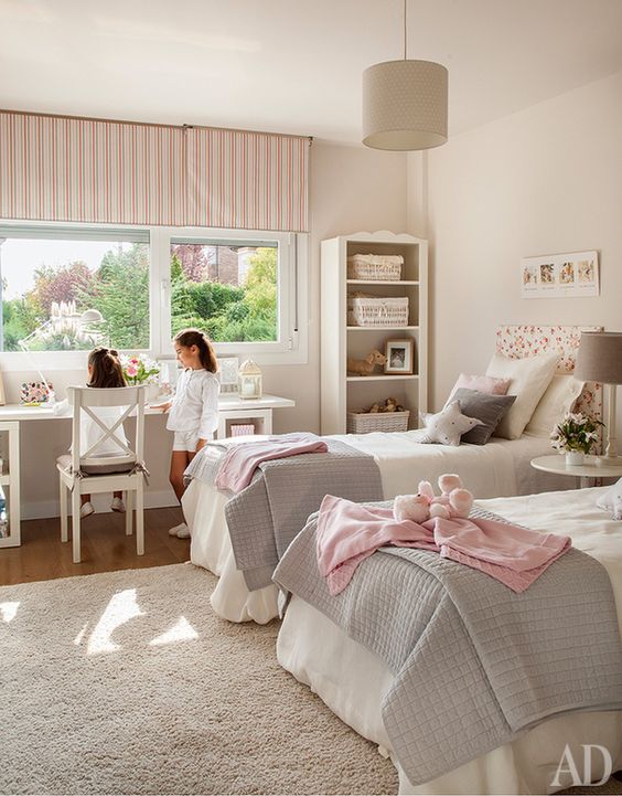 a cool neutral shared girls' bedroom with vintage furniture, a desk by the window and chairs, pink and grey textiles and lamps
