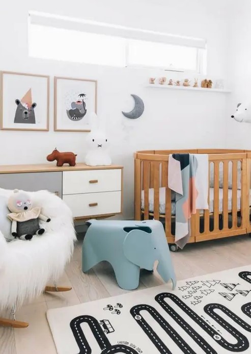 a cozy Scandi nursery with a stained crib, a stained dresser, a faux fur chair, a blue elephant chair, some artworks and a play rug