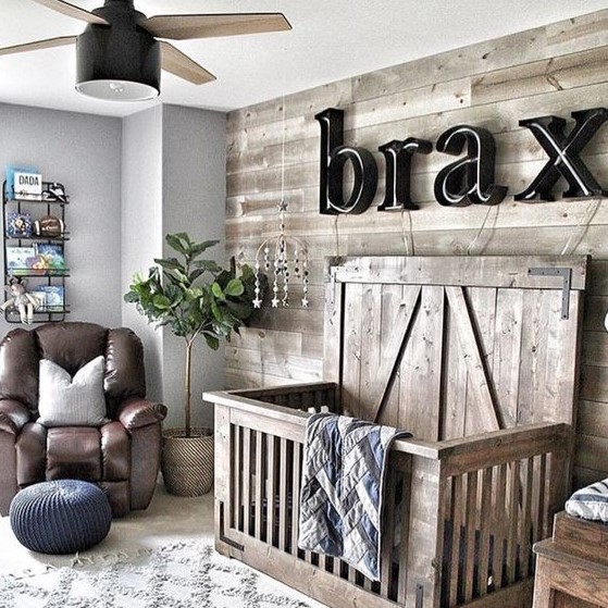 a cozy farmhouse nursery, a reclaimed wood wall and a matching crib, a name on the wall, a leather chair and a lamp fan