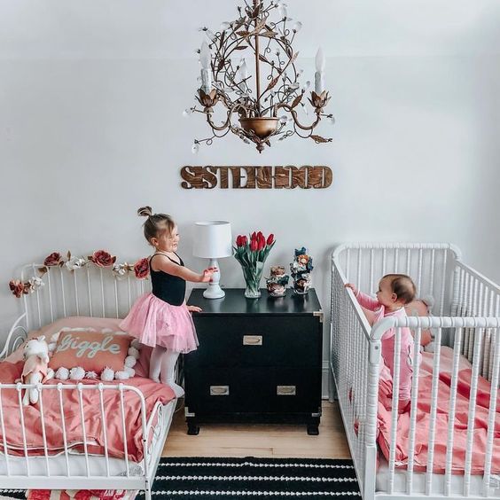 a cute black and white shared room with white beds, pink bedding and whimsy and chic details