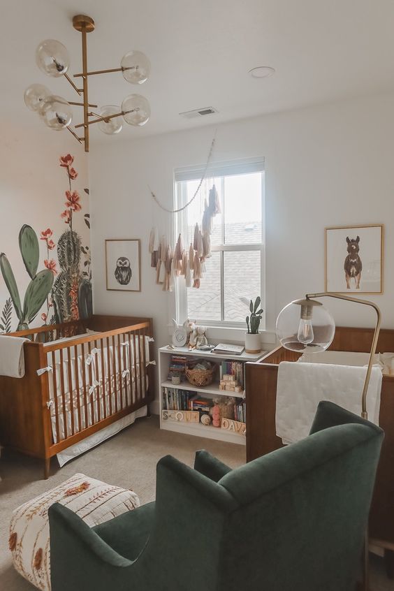 a desert themed nursery with stained cribs, a hunter green chair, a tassel hanging and a cactus accent wall