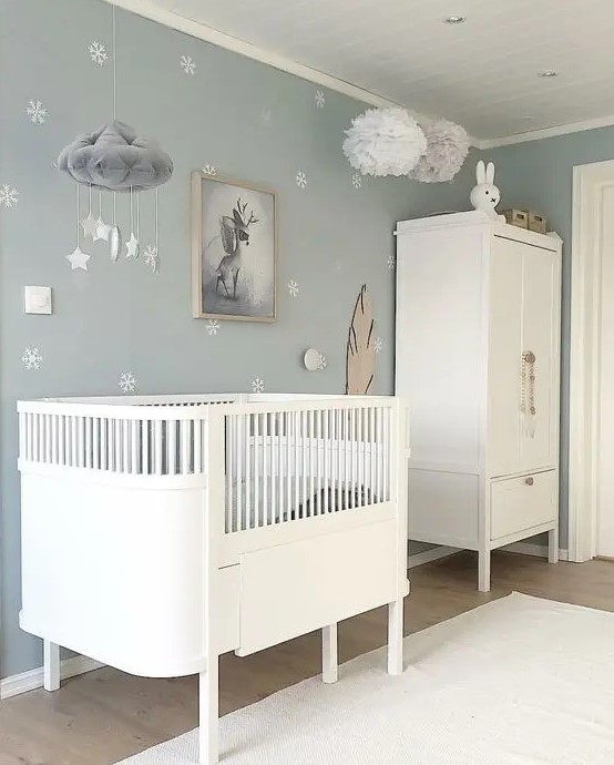 a dreamy Scandi nursery with pale blue walls and an accent one, white furniture, pendant lamps and a mobile plus toys