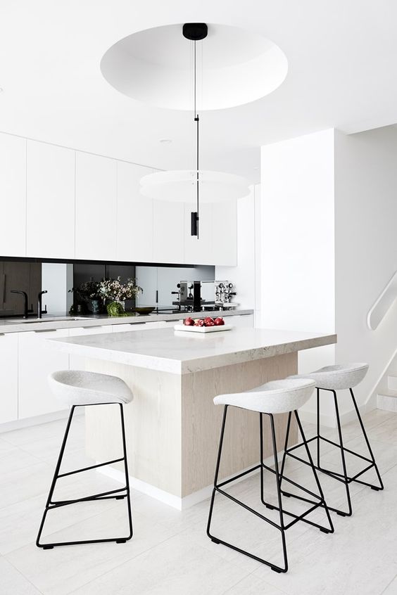 a fantastic minimalist kitchen with sleek white cabinets, white stone countertops, a black glass backsplash and black pendant lamps