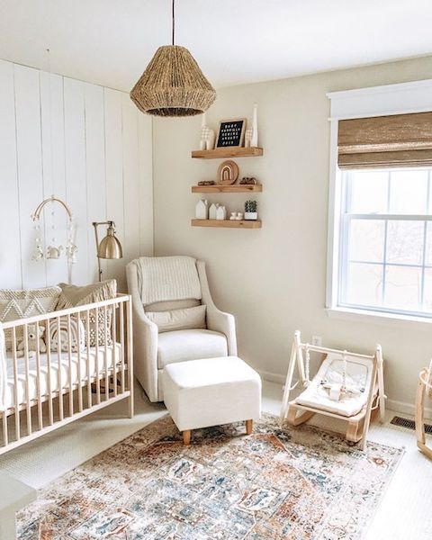 a farmhouse neutral nursery with light-colored furniture, a boho rug, a woven lamp and wooden furniture