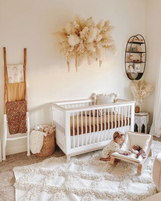 a gender neutral nursery done in warm neutrals, with white and neutral furniture, pampas grass, toys and layered rugs