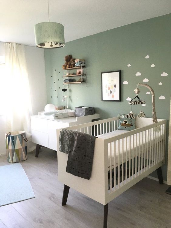 a gender neutral nursery with a green wall, minimal and sleek furniture, a green pendant lamp and some art and accessories