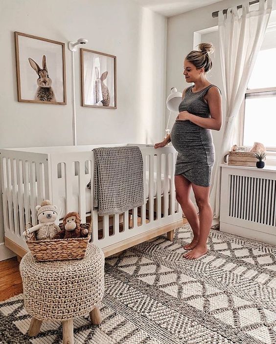 a gender neutral nursery with bunny artworks, a woven rug and ottoman on wooden legs is ultimate cuteness and chic