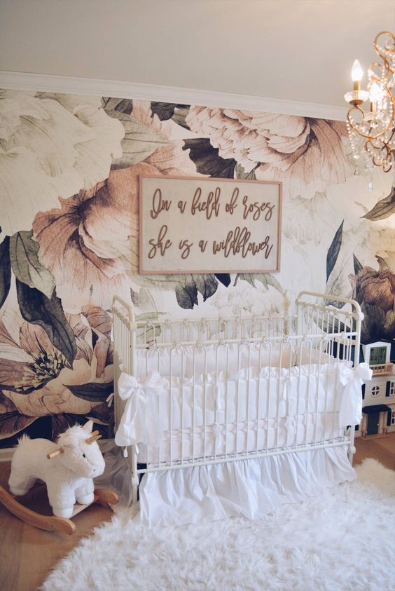 a glam nursery with a floral wallpaper wall, white furniture, a crystal chandelier and white bedding and textiles