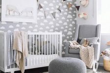 a grey gender neutral nursery with a cloud accent wall, chic white and grey furniture and garlands and faux taxidermy
