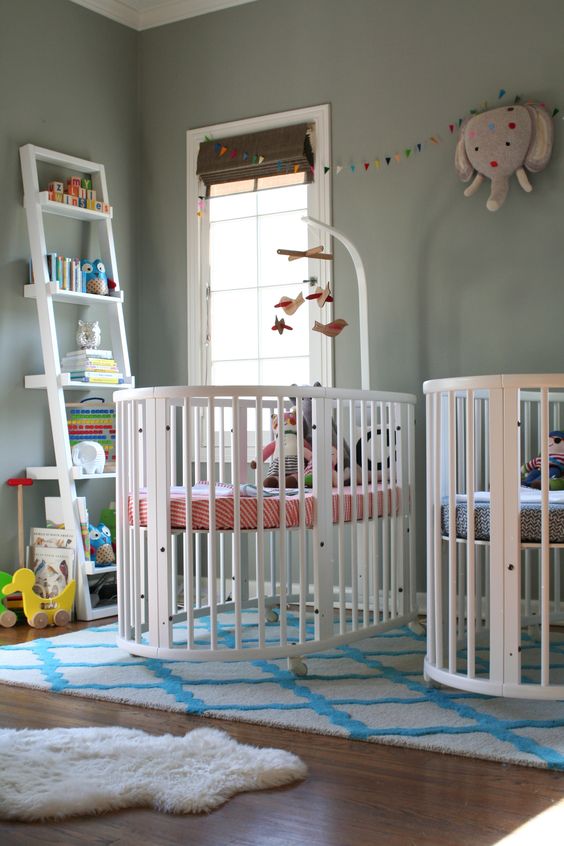 a grey nursery with white furniture, colorful and printed linens and a bookshelf with colorful books and toys