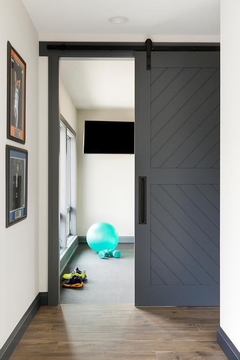 a grey sliding barn door hides a small private gym and saves some space at the same time