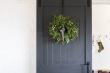 a grey sliding barn door with handles with a large greenery wreath brings a cheer holiday feel