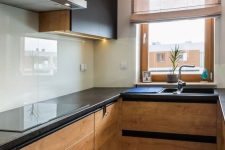 a light-stained and black modern kitchen with black countertops and a neutral glas sbacksplash plsu stainless steel appliances