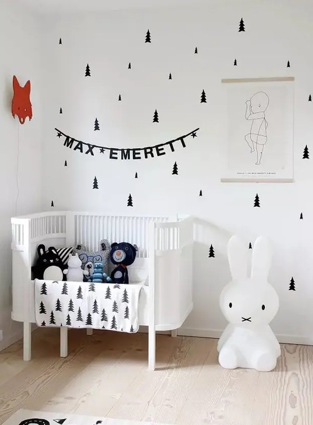 a lovely Scandi nursery with tree decals, a white crib, an iconic Miffy lamp, some art and lots of toys