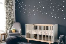 a lovely nursery with a black celestial accent wall, a white crib, a grey chair, a blue rug and some lovely toys