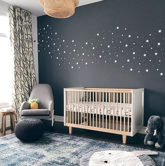 a lovely nursery with a black celestial accent wall, a white crib, a grey chair, a blue rug and some lovely toys