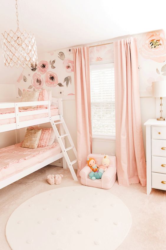 a lovely shared girls' bedroom with pink floral walls, a bunk bed, a white nightstand, pink textiles and some cute toys