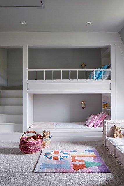 a minimalist shared girls' bedroom with bunk beds and built-in shelves, a sofa by the window and bright printed textiles