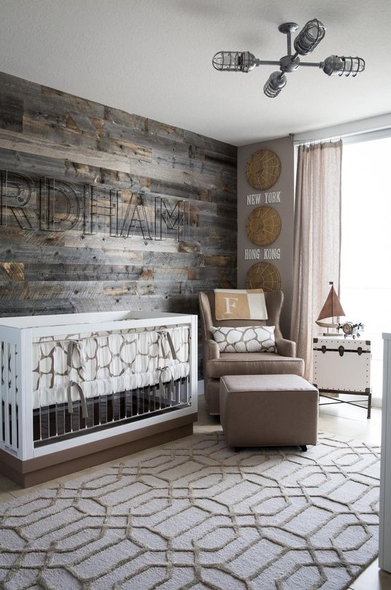 a modern farmhouse nursery with a reclaimed wooden wall, a taupe chair and footrest, a modern crib with acryl and a printed rug