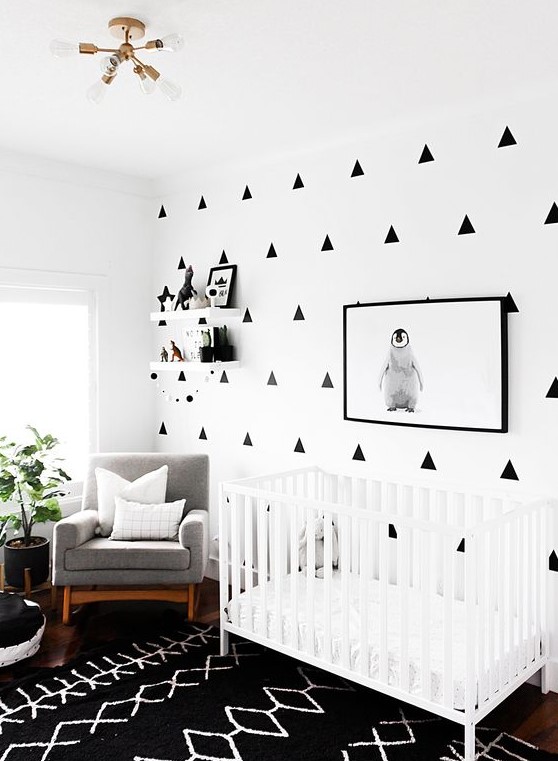 a modern monochromatic nursery with a geo printed wall, a printed rug, a white crib, a grey chair and a potted plant