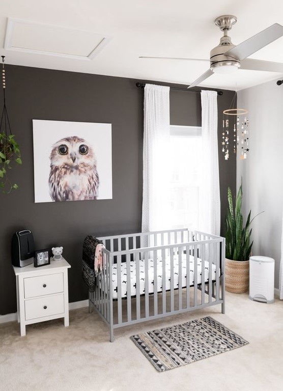 a modern nursery with a black accent wall, a grey crib, potted plants, a printed rug and neutral curtains is very cool