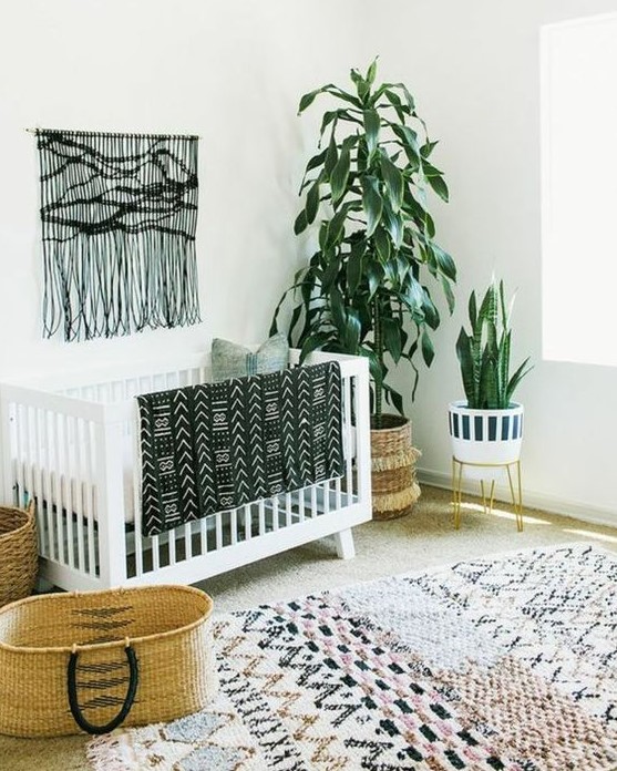 a monochromatic boho nursery with a black macrame hanging, a printed rug, a folksy print blanket and potted plants