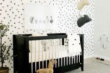 a monochromatic nursery with a geo accent wall, a black and white crib, a neutral rug and faux taxidermy plus potted plants