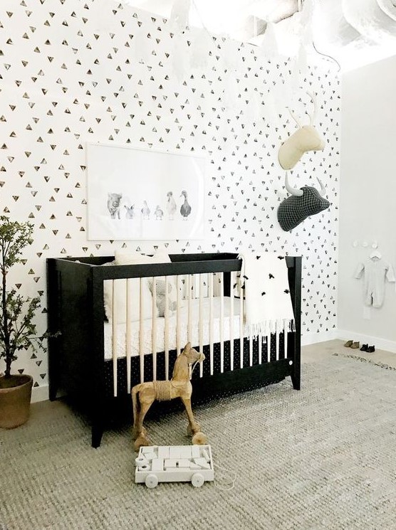 a monochromatic nursery with a geo accent wall, a black and white crib, a neutral rug and faux taxidermy plus potted plants