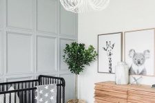 a neutral nursery with a grey paneled accent wall, a black crib with white and grey bedding, a catchy wooden dresser and a mini gallery wall