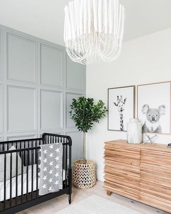 a neutral nursery with a grey paneled accent wall, a black crib with white and grey bedding, a catchy wooden dresser and a mini gallery wall