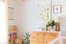 a neutral nursery with light stained furniture, a rattan lamp, colorful artworks and colorful books