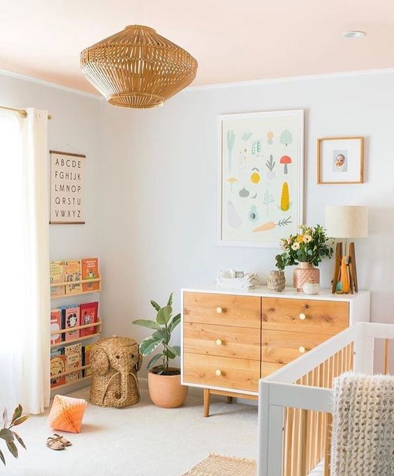 a neutral nursery with light stained furniture, a rattan lamp, colorful artworks and colorful books