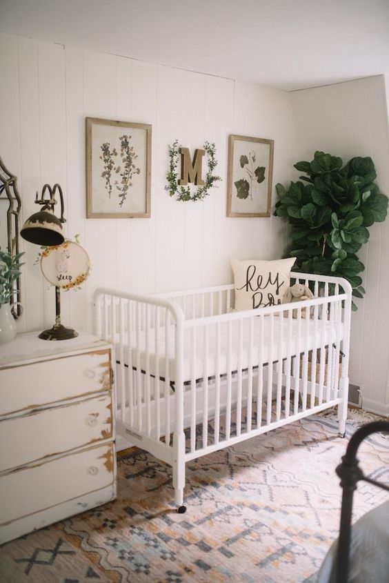 a neutral vintage nursery with white shabby furniture, a statement plant, artworks and a vintage lamp