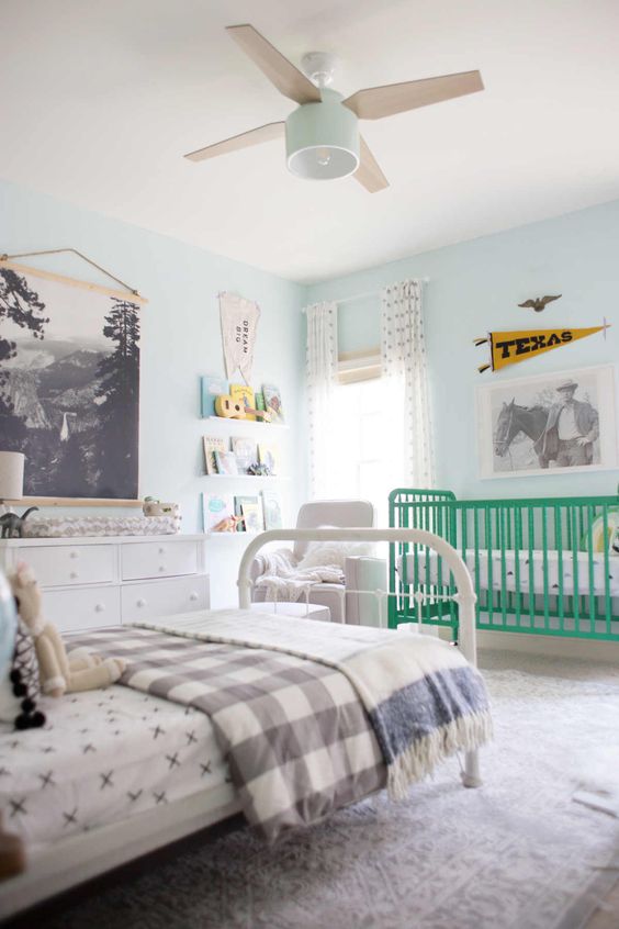 a pastel shared nursery with light blue walls, a green crib, a white bed and other furniture and cool artworks