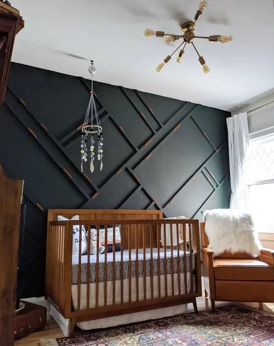 a pretty and small mid-century modern nursery with a black paneled wall, a stained crib, an amber leather chair, neutral textiles, a chandelier and a mobile