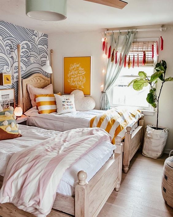 a relaxed and welcoming shared girls' bedroom with stained wooden beds, printed and neutral bedding, an accent wave wall, tassels and curtains, a mint pendant lamp