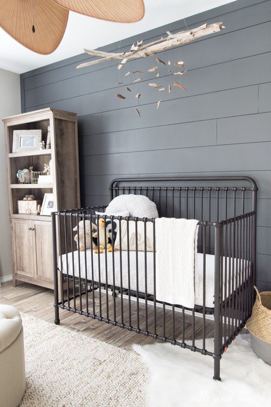 a rustic gender neutral nursery with a grey accent wall, a reclaimed wood storage unit and a black metal crib