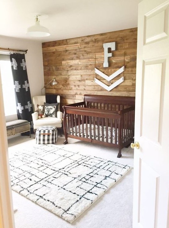 a rustic nursery with a printed rug, a stained crib, a reclaimed wall and some touches of prints