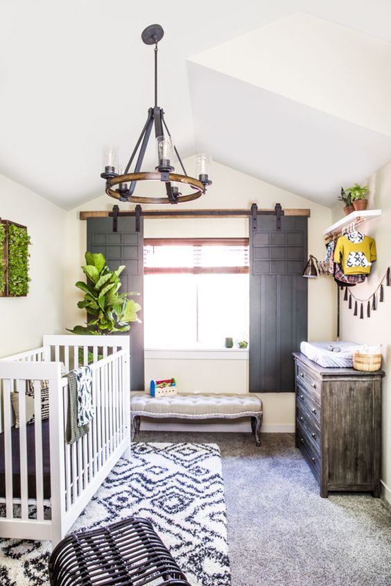 a rustic nursery with sliding shutters, a wooden chandelier, a weathered dresser and prints is a welcoming space