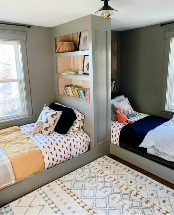 a shared girls' bedroom with grey walls, beds separated with a bookcase, printed textiles is a lovely and cozy space