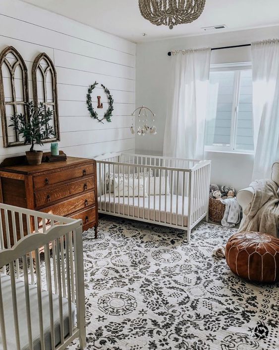 a shared nursery with shiplap walls, a stained dresser, a leather ottoman and a beaded chandelier
