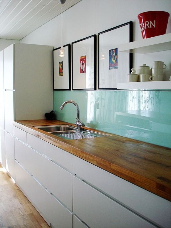 a sleek modern white kitchen with butcherblock countertops, a bold mint glass backsplash and open shelves instead of cabinets