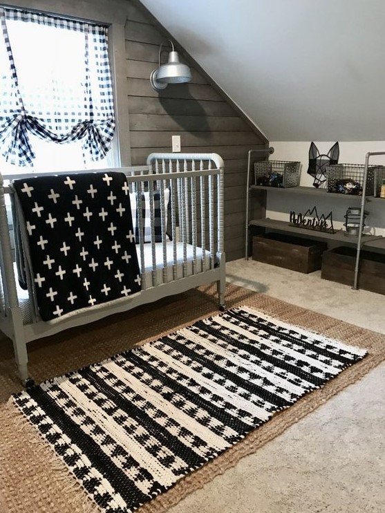 a small attic nursery with a jute rug, a printed one, a grey vintage crib, prints and a reclaimed wooden wall