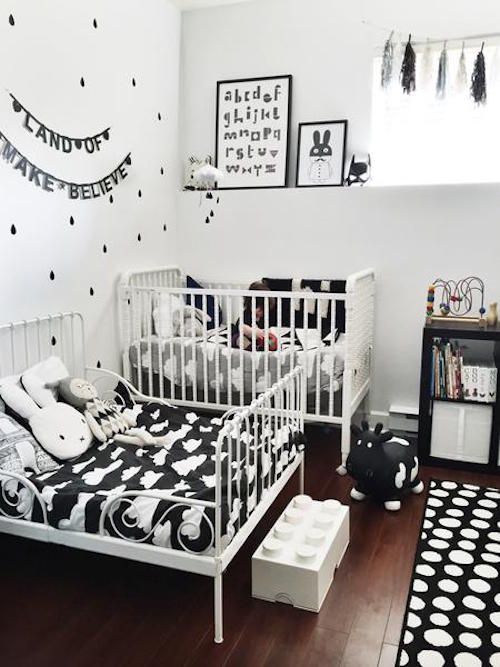 a small black and white shared room with some fun prints, cute toys and textiles plus a bunting