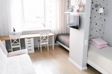 a small shared kids’ bedroom with beds by the walls and a space divider, a double desk with chairs and a sofa plus a TV